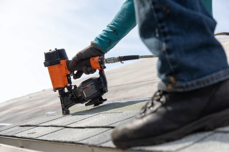 man installing new shingles on the roof using nailgun
